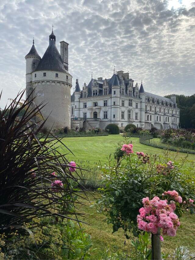 Chateau Chenonceau, one of the best Loire Valley Castles, with a garden with pink flowers under cloudy skies