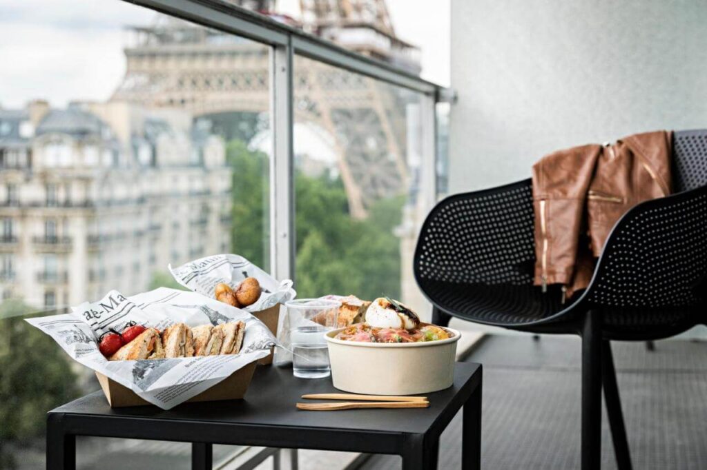 A balcony of a hotel and food on a table with a chair overlooking the Eiffel Tower in Paris in October
