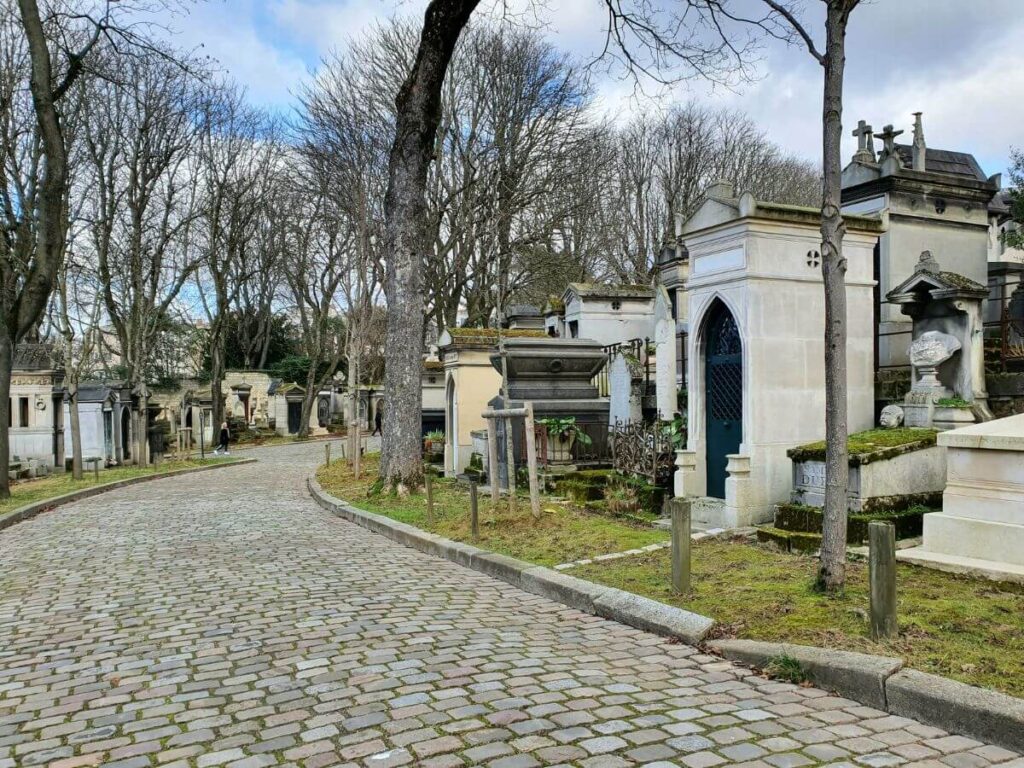 The cobbled stone path of the Père-Lachaise Cemetery with tombstones on the side in Paris in October