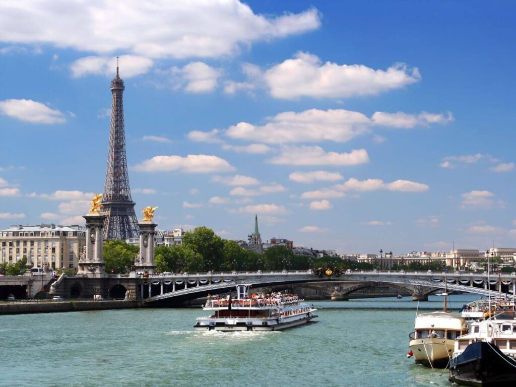 A white boat cruise heading towargds a a bridge with a view of the eiffel tower in the back under bright skies in Paris in October