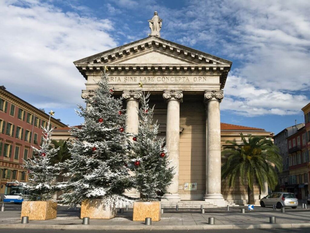 Christmas trees covered in snow in front of the La Place I'lle de Beaute in Nice, one of the best places to visit in France in winter
