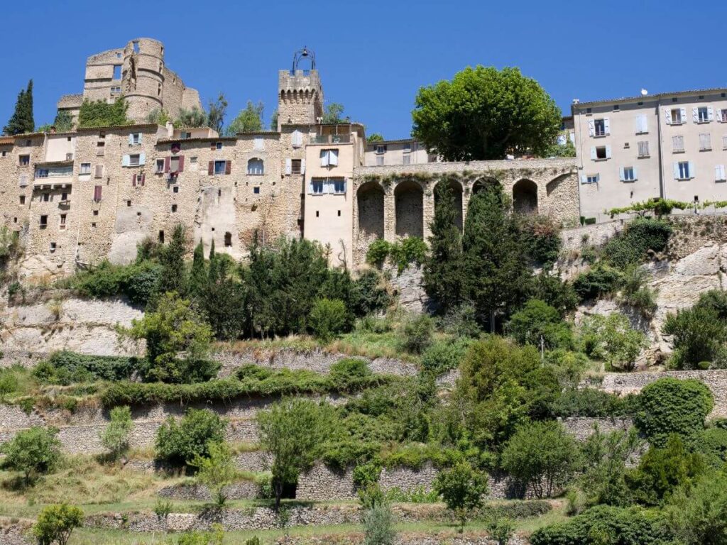 Montbrun-les-Bains en Sault Provenza con edificios de piedra con arbustos y árboles delante