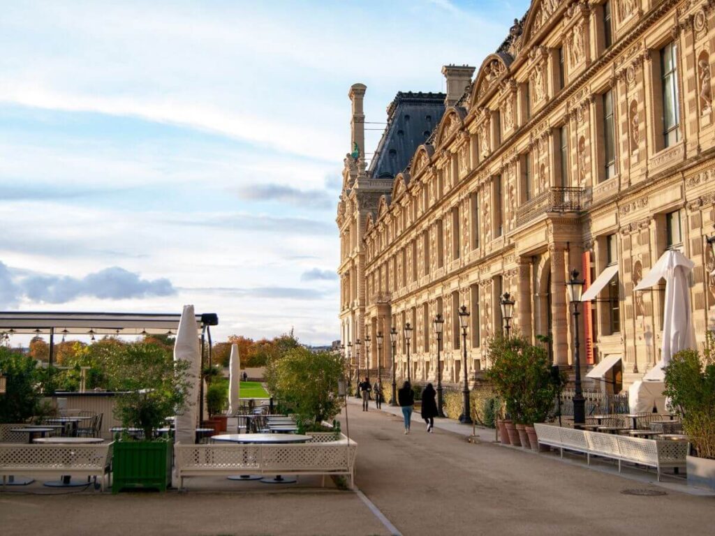 An outdoor space with tables and chairs and people walking outside the Musée des Arts Décoratifs, one of the best fashion museums in Paris