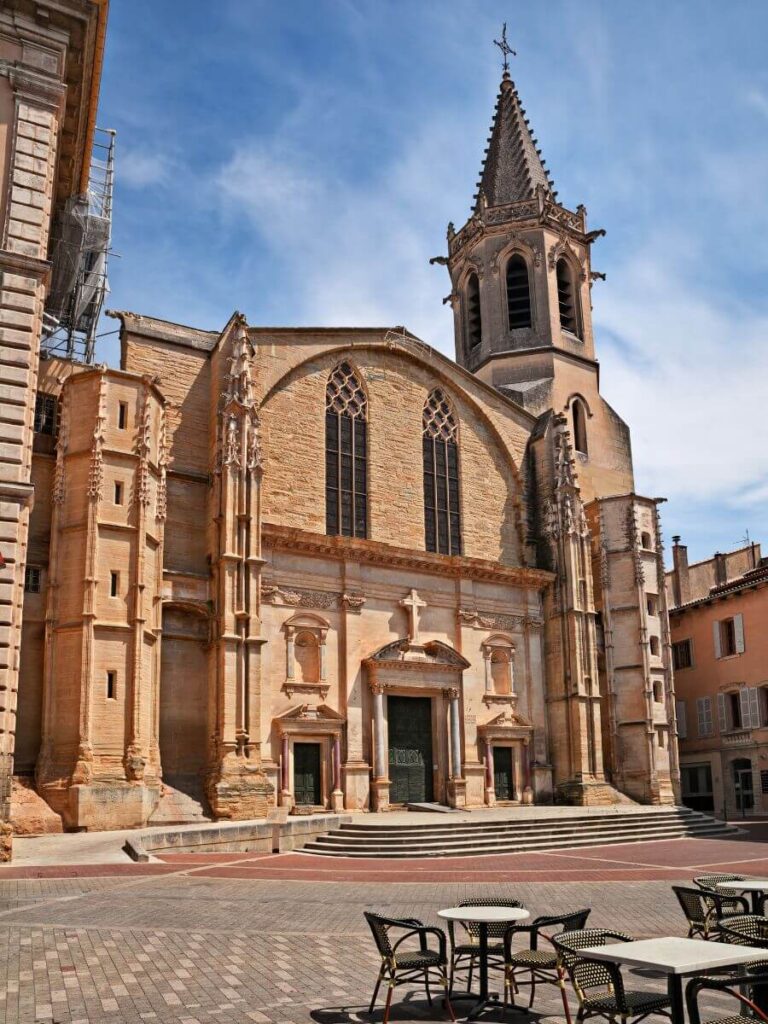 El espacio exterior de la Cathédrale Saint-Siffrein con mesas y sillas en primer plano en Carpentras, cerca de Sault Provence