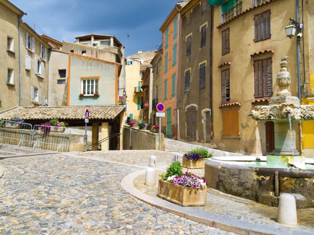 fountain surrounded by buildings in warm colors and a fountain and boxes of flowers in Valensole Provence France