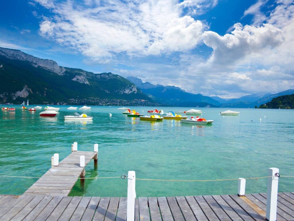 Las aguas cristalinas del lago de Annecy bajo un cielo nublado y pequeñas embarcaciones en el agua