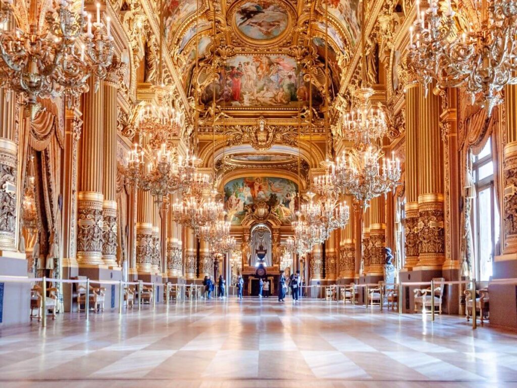 Large lighted chandeliers hanging from the ceiling with frescoes in Grand Opéra Garnier Foyer in Paris in October