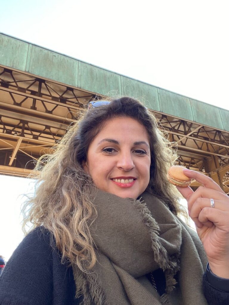 Vero Holding a macaron while wearing  scarf, an essential for the Paris packing list